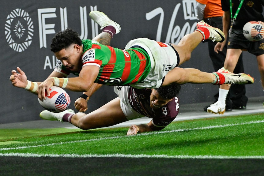 A South Sydney NRL player's whole body is in the air as he stretches out his hand to plant the ball for a try. 