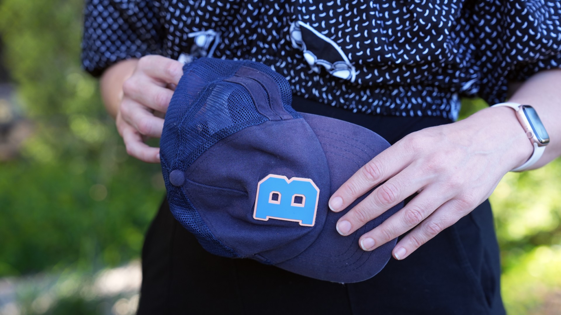 Woman's hand holding a hat that is dark blue with a light blue letter B on it