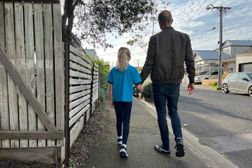 A man and young girl walking along a suburban street. 