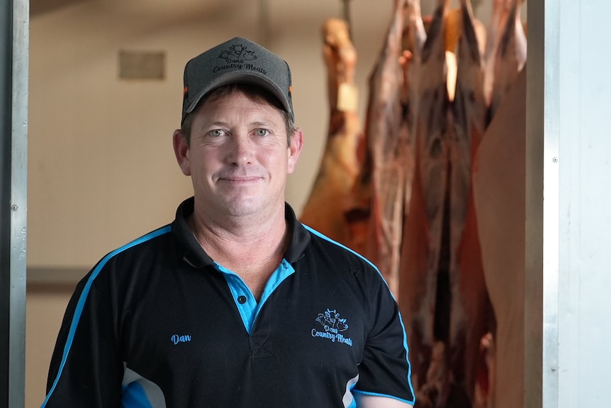 Butcher Dan Walton smiles at camera standing in front of meat storage