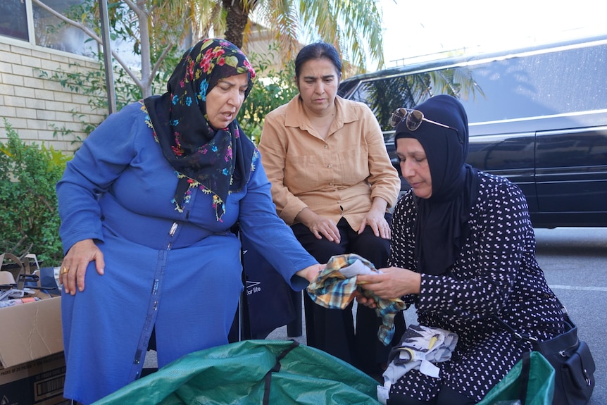 Three Turkish women are seated, sorting clothes.
