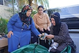Three Turkish women are seated, sorting clothes.