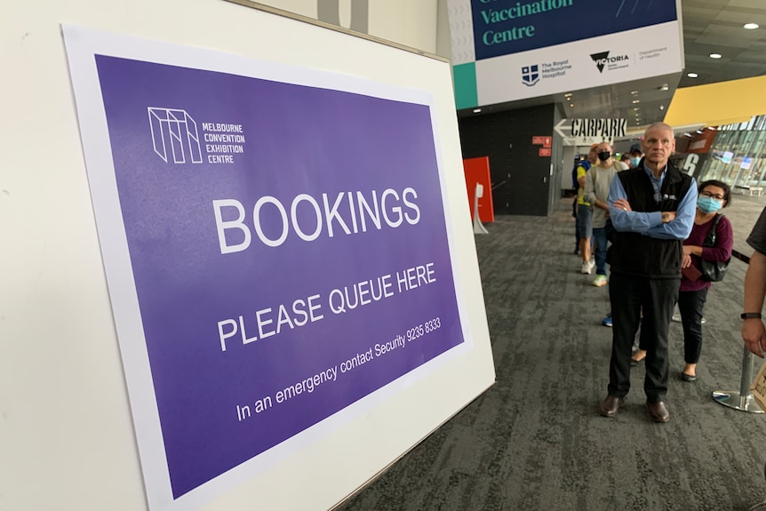 A large purple booking sign with a blurred queue of people in the background.