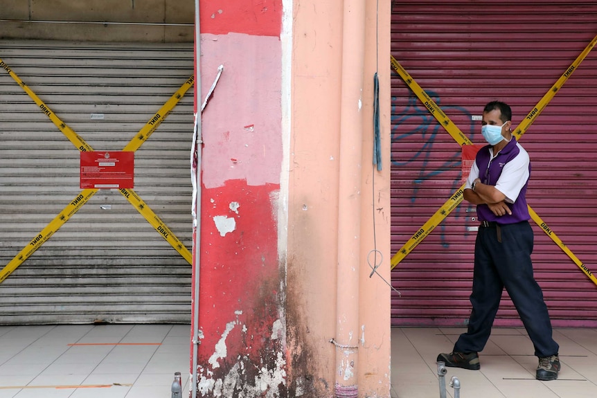 A man wearing a protective mask walks past closed shops in Kuala Lumpur, Malaysia.