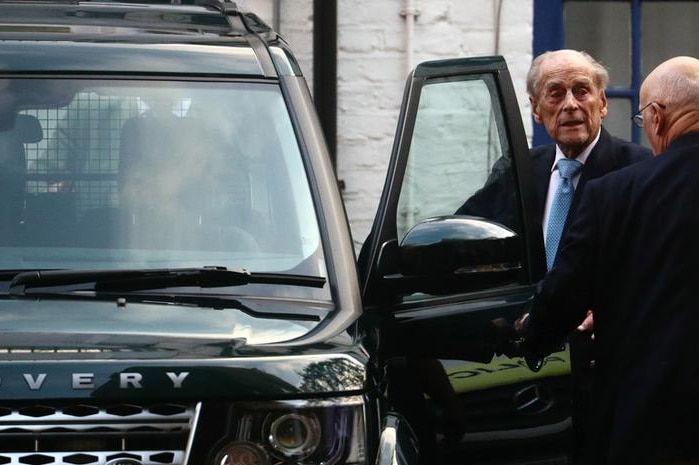 Prince Philip looks straight ahead as he gets into a black Range Rover. A man holds the car door out to him and faces him.