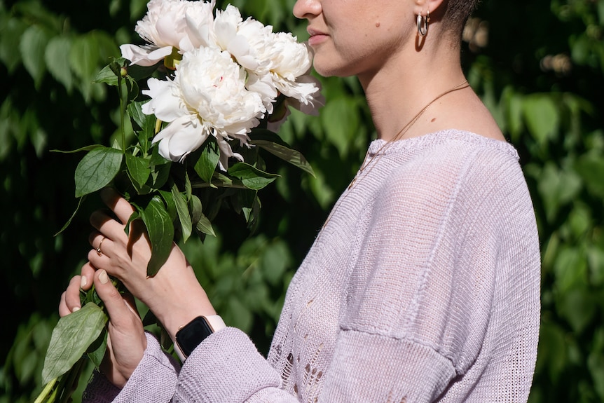Barbara holds a white bunch of flowers, smelling them with her eyes closed