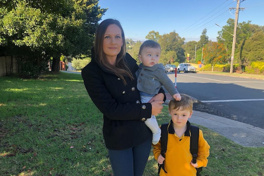 lady holds toddler next to boy in school uniform