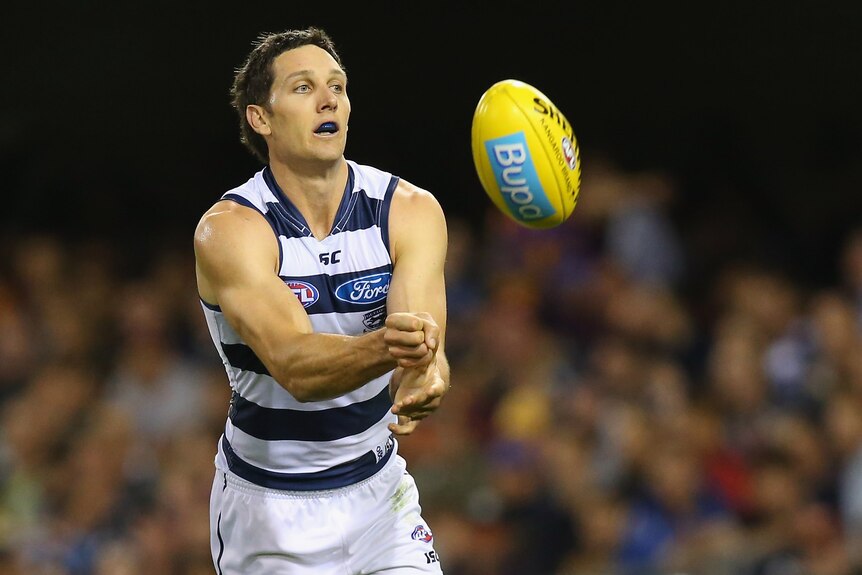 A Geelong AFL player watches the ball fly away as he clenches his fist after delivering a handball.he 