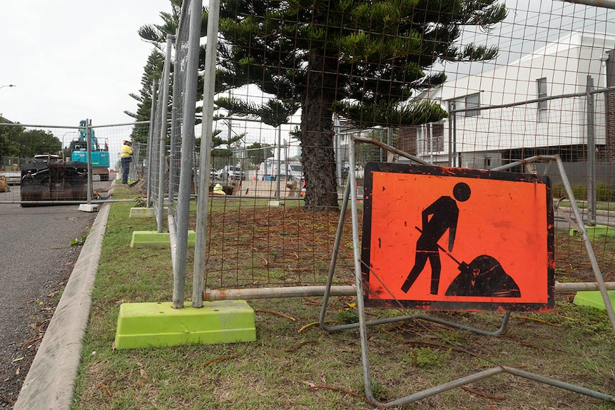 A road sign showing a men at work symbol in front of cyclone fencing on a median strip