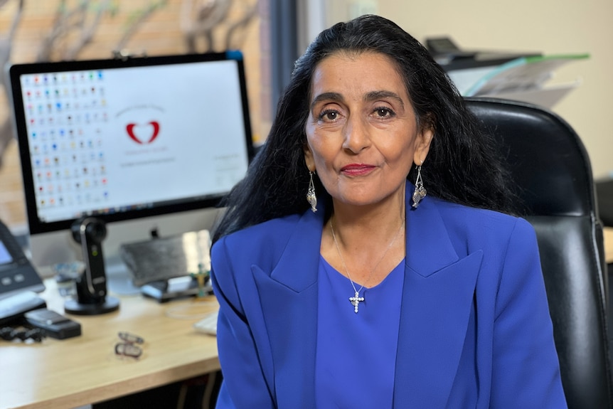 A woman smiles softly, sitting at her office desk.