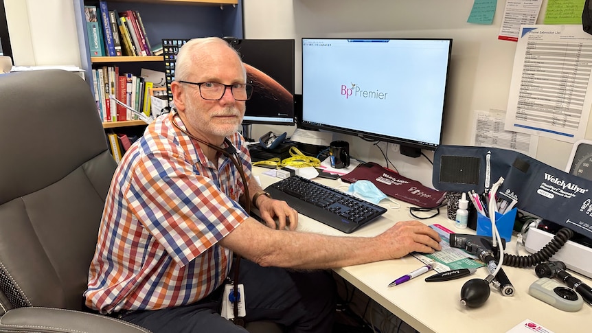 Dr McPhee sits at a desk with a computer.