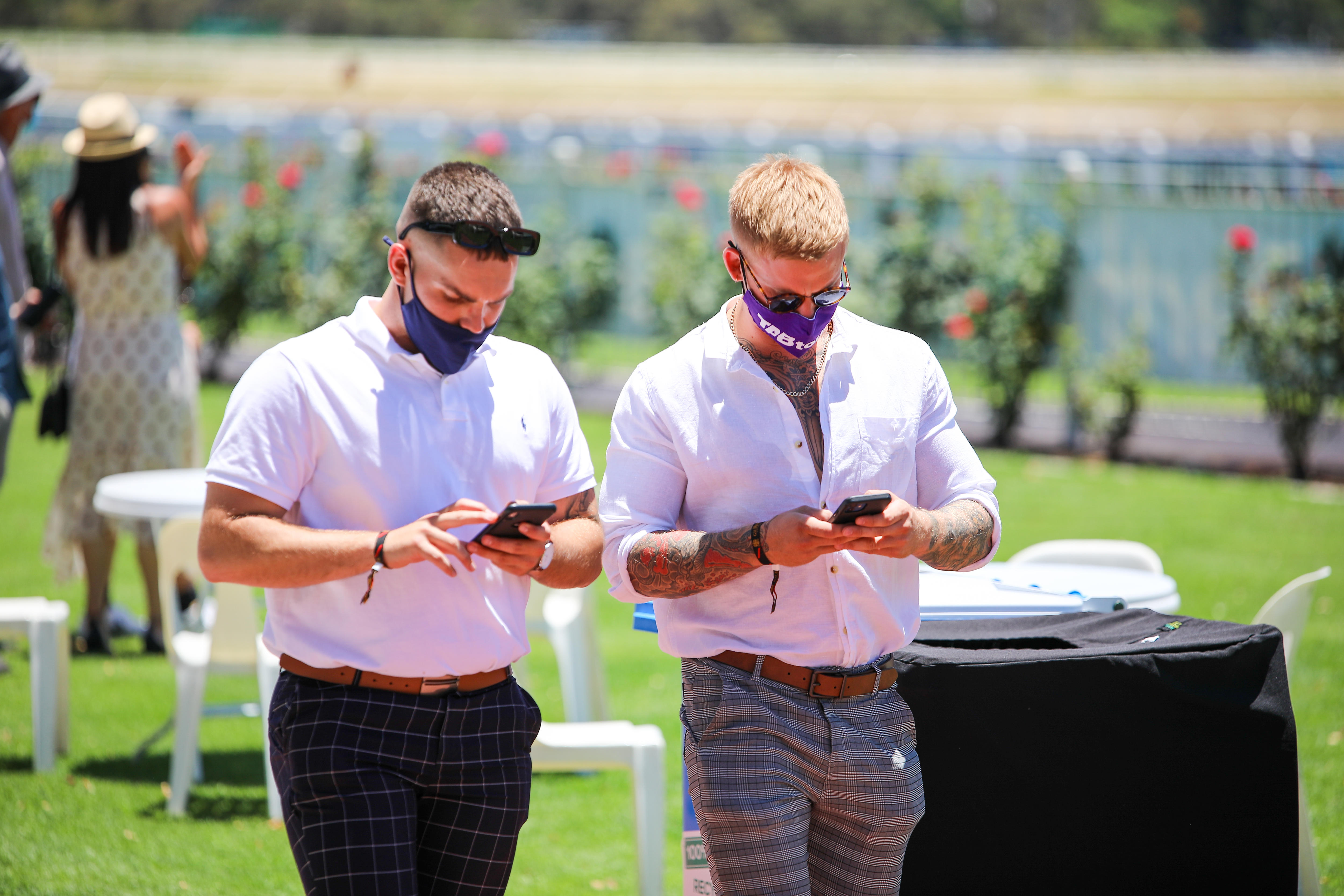 Two men in formal wear walk along a racecourse
