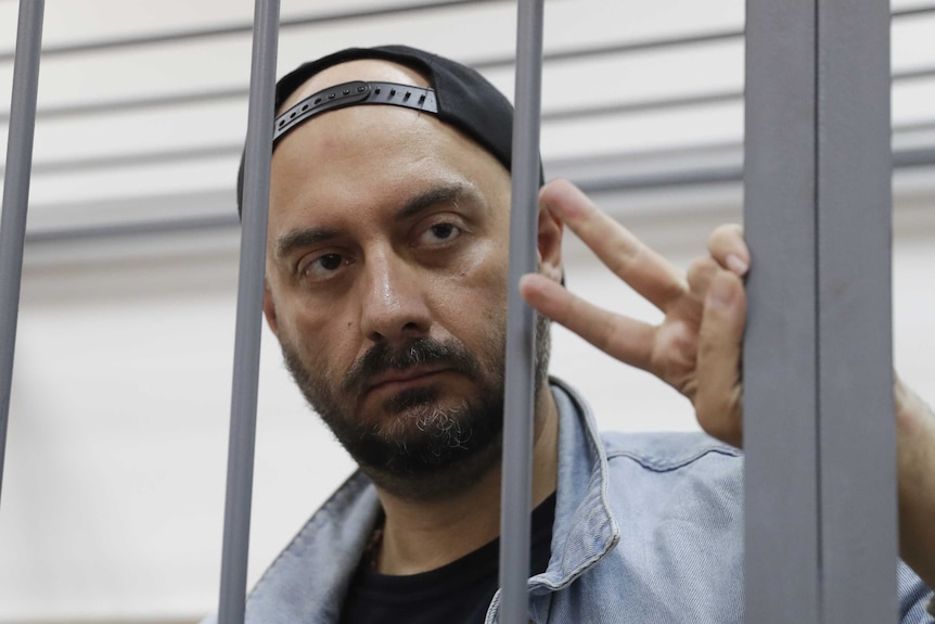 A man wearing a cap backwards gives a peace sign from behind bars.