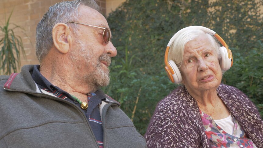 Ken looks at Nancy who is wearing a set of headphones.