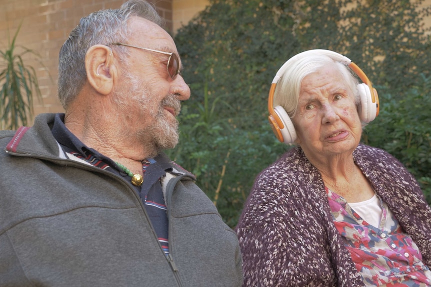 Ken looks at Nancy who is wearing a set of headphones.