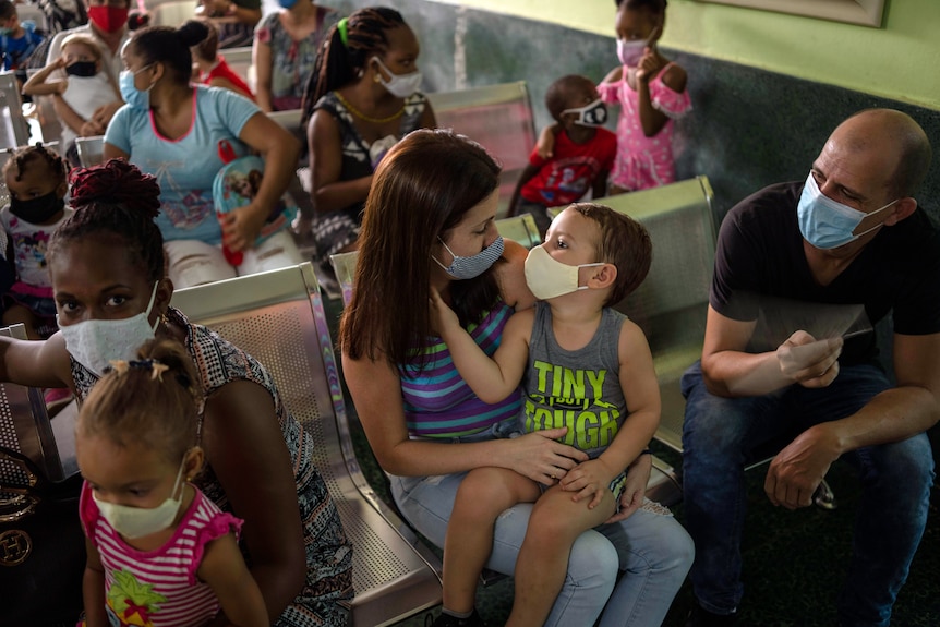 A group of parents with their children wear masks as they sit on chairs.