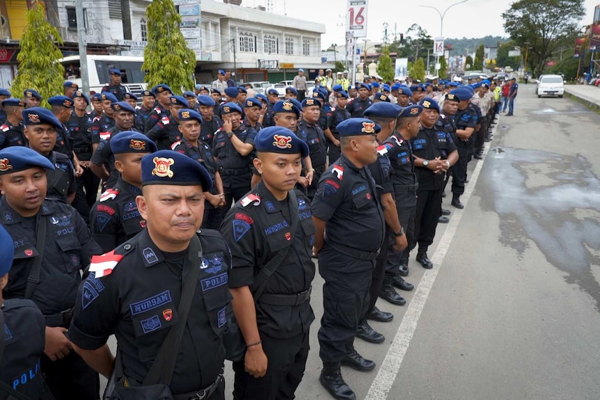 Police in dark uniforms and berets stand in rows on a street in West Papua.