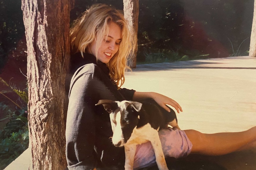 A blonde teen looks down at a dog with a smile