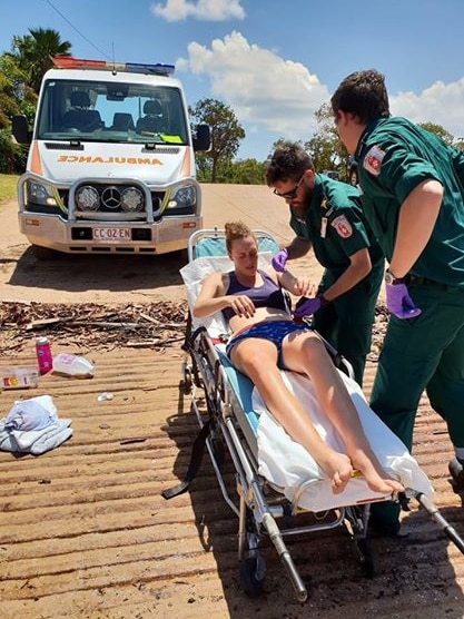 Paramedics assist a young woman on a stretcher.