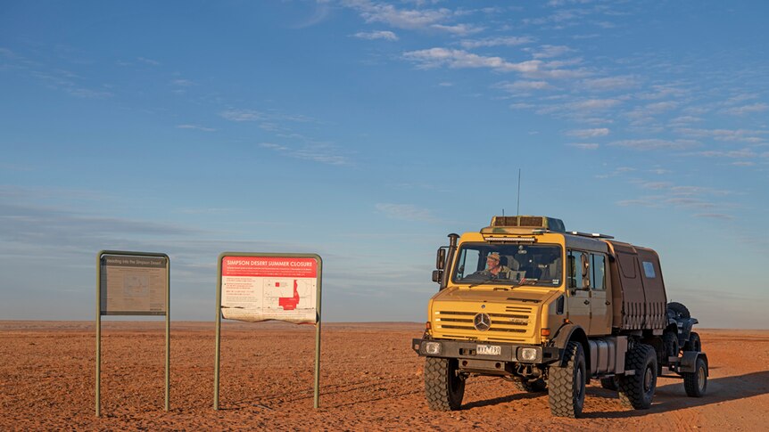 Large yellow truck driving through Simpson desert past sign saying Simpson Desert