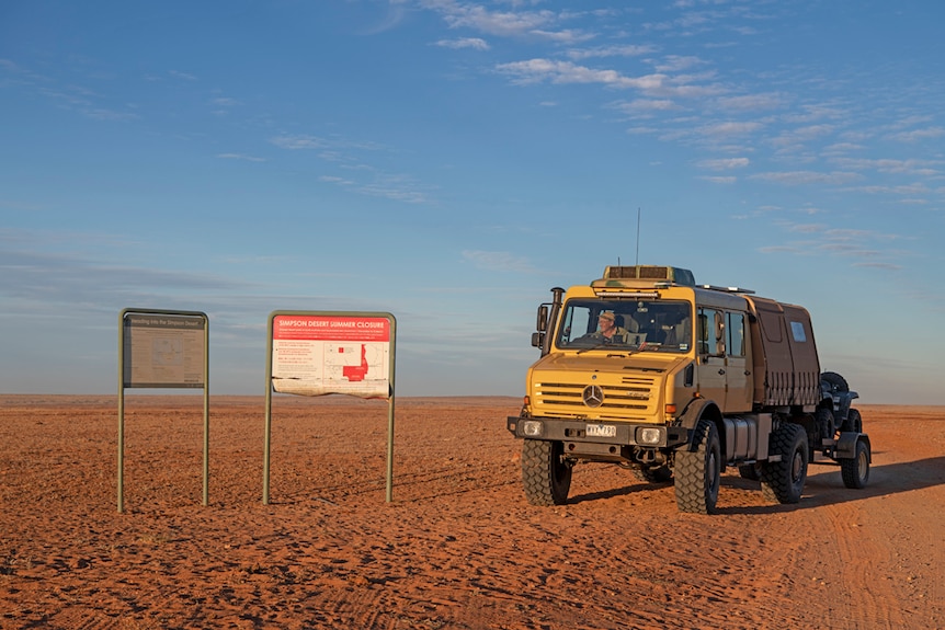 Large yellow truck driving through Simpson desert past sign saying Simpson Desert
