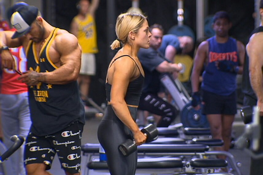 A woman holding weights in a busy gym.