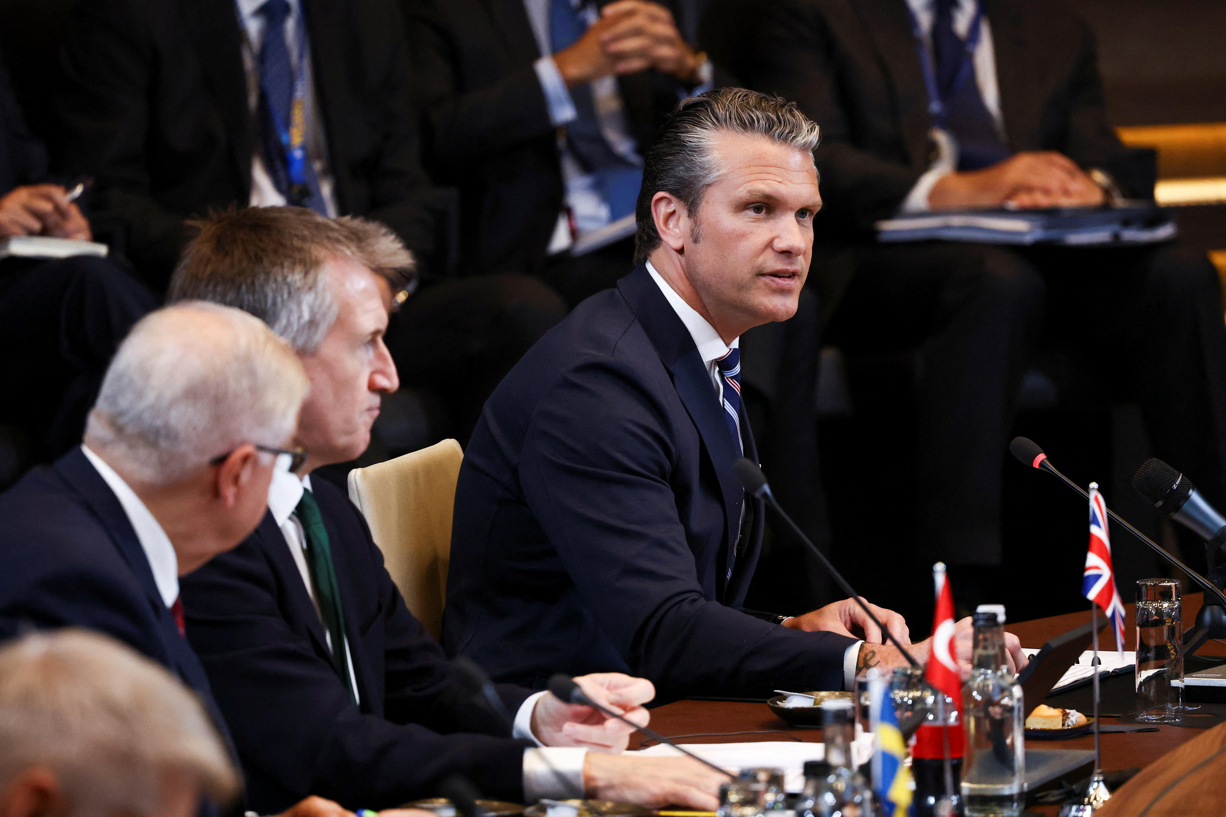 Pete Hegseth speaks to a NATO conference while sitting down