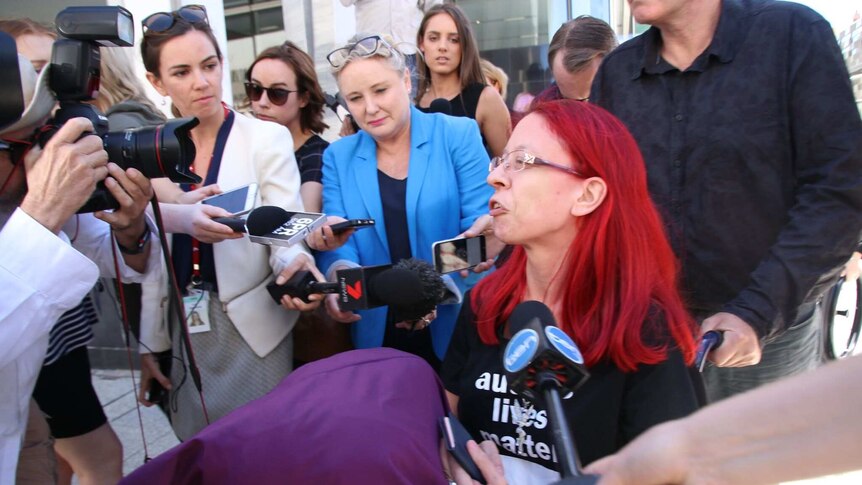 A woman with red hair speaks to a large media pack outside court.