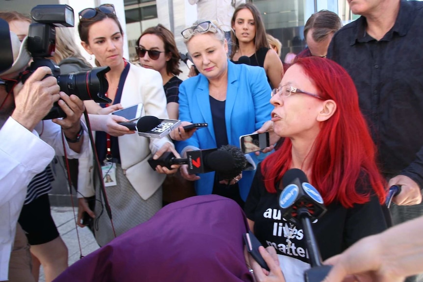 A woman with red hair speaks to a large media pack outside court.