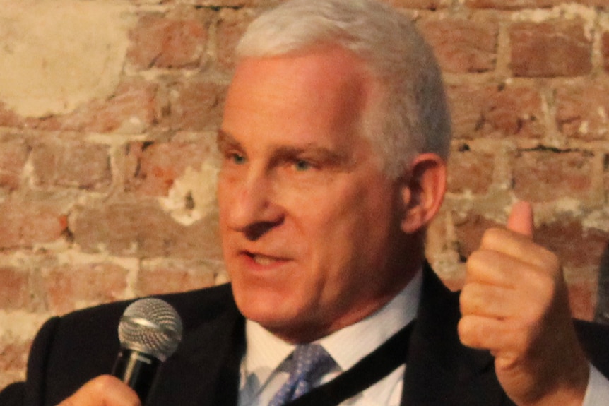 a man in a suit holding and speaking into a microphone