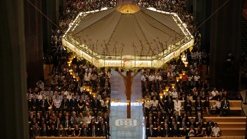 An illuminated statue of Jesus on the cross hangs above people attending a mass for the Barcelona terror attack victims.