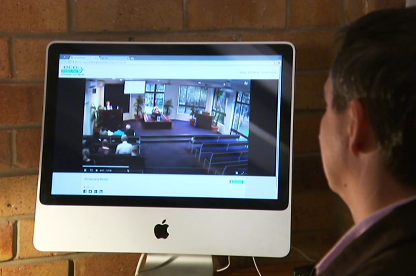 A man watches a computer screen with an image of a chapel on it.