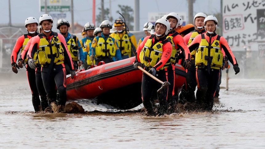 Japanese recsue team carry an inflatable raft through flood waters.