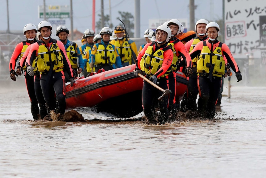 Japanese recsue team carry an inflatable raft through flood waters.