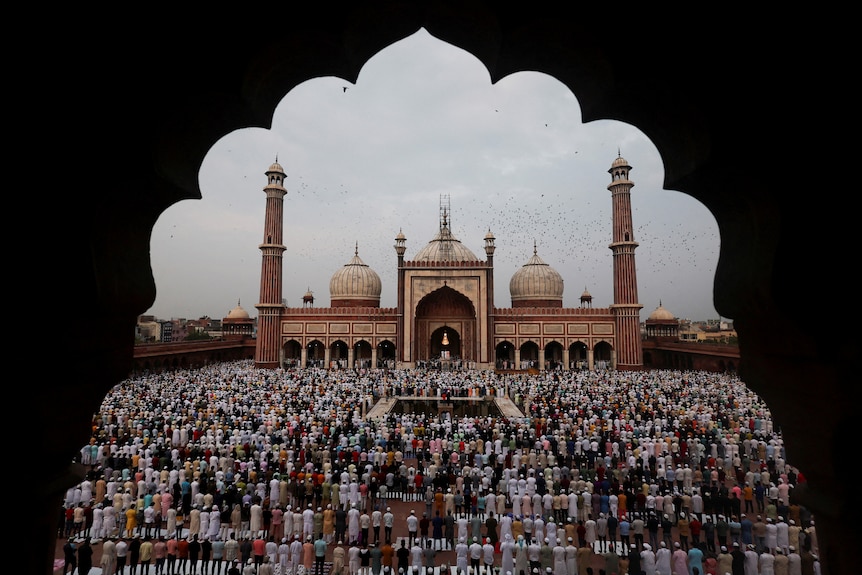 A picture of many people praying in front of a mosque