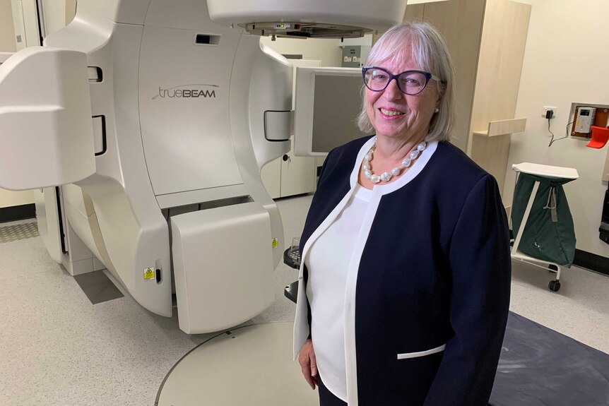 Dr Marie Burke smiles in front of a radiation machine.