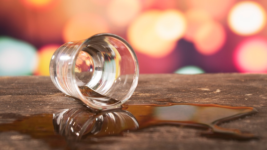 glass with liquid spilt across table against unfocused lights