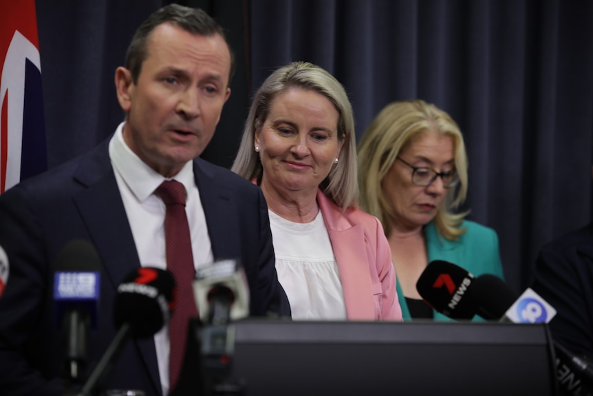Mark McGowan speaks at a media conference wearing a blue suit and red tie, with his wife Sarah and Rita Saffioti behind him.