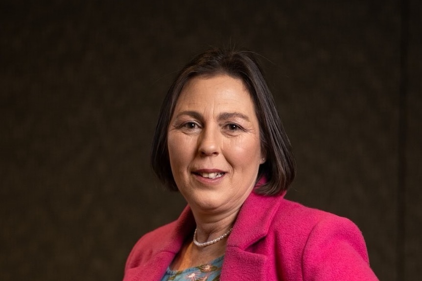 Professional picture of a middle-aged woman in a pink blazer, with short brunette hair, smiling at camera