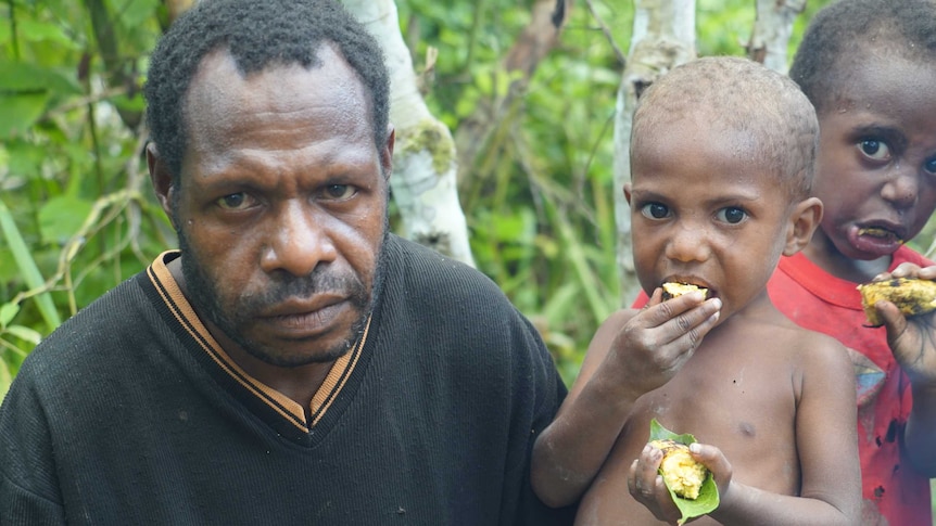 Two young Tumam boys eat as they stand next to a man