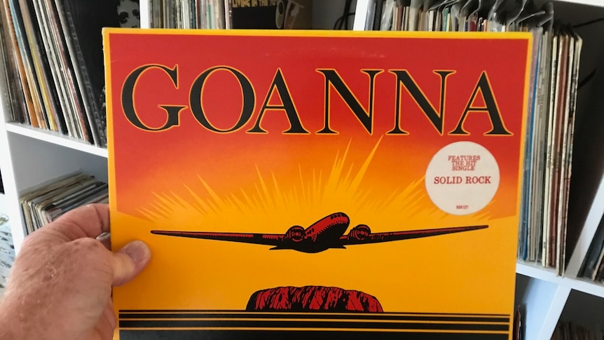 A record cover with the word GOANNA and a red and yellow image of Uluru is held in someone's hand.