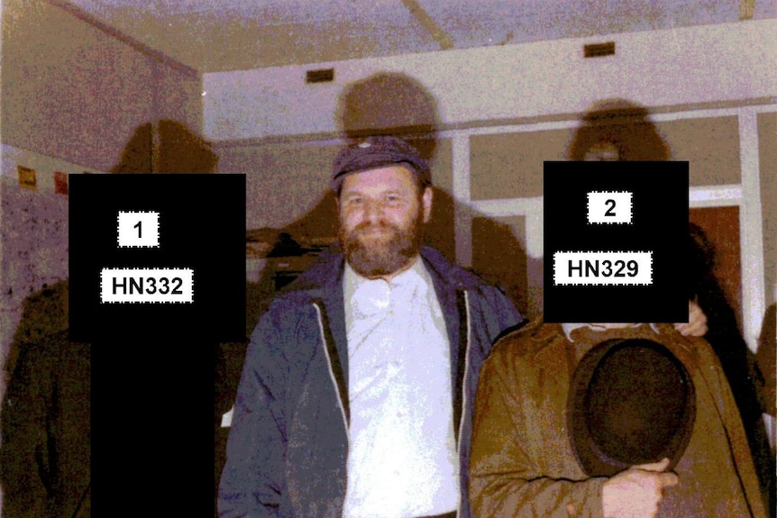 An old photo of a man with a beard standing between two other men whose face have been obstructed with black squares