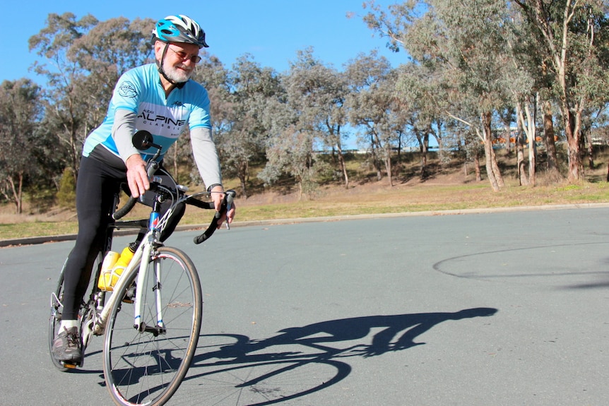 Elderly man rides a road bike around a roundabout in front of parkland.