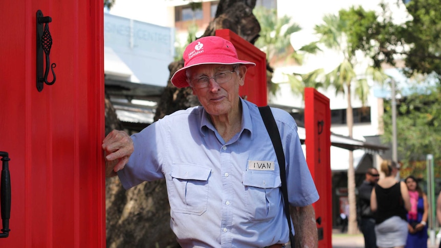 An elderly man standing next to several red doors.