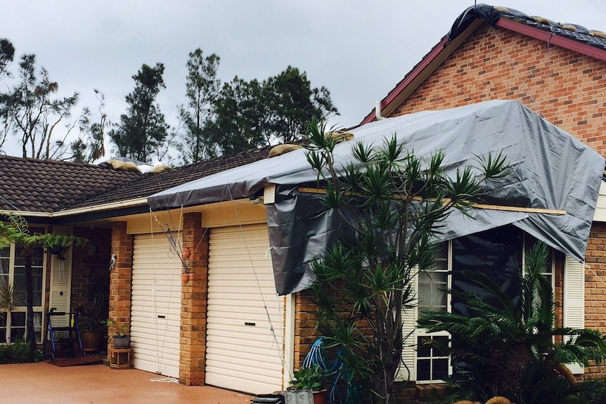 A grey tarpaulin partially covering the garage and roof of a brick house in Kurnell.