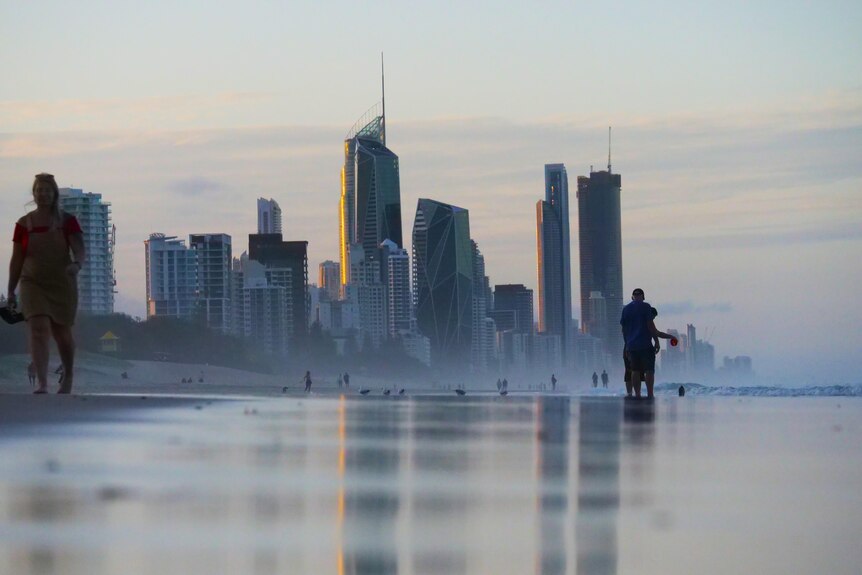 Tall towers reflect in water at a beach.