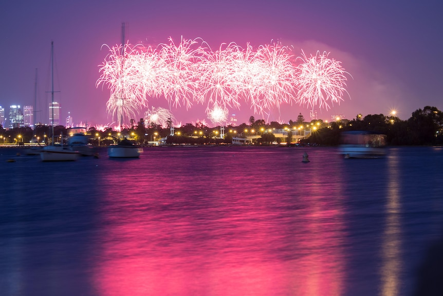 Pink and purple coloured fireworks explode over water