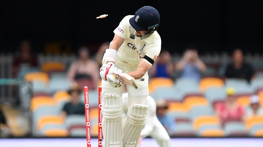 An English batsman turns his head mid-shot as the bails fly in the air behind him as he is clean bowled.