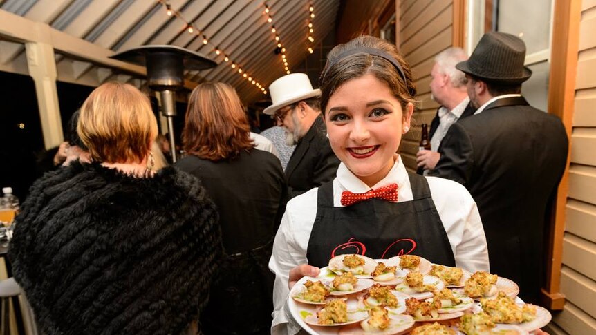 A female waiter holds a platter of scallops up to the camera.