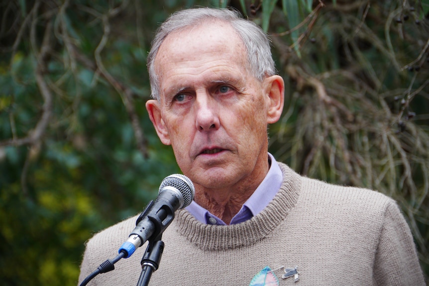 A close up of a man wearing a beige sweater standing in front of a mic